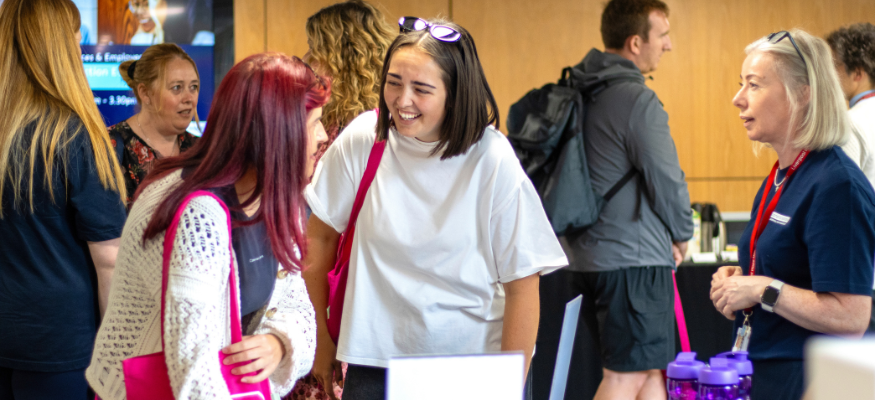 Apprentices laughing together as they sign in to their induction event in a busy room